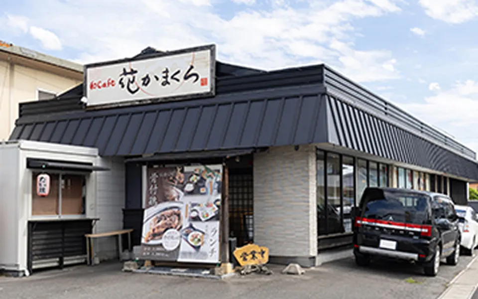 「花かまくら」の店舗外観。黒い屋根と白い看板が特徴的な和食レストランで、入口にはランチメニューのポスターと営業中の看板が置かれている
